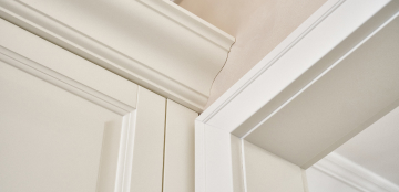 Close-up of white ceiling molding showing a visible crack where it meets the wall. The bright lighting emphasizes the clean, smooth lines of the molding.