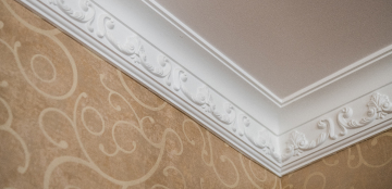Ornate white crown molding meets textured beige walls with swirling patterns, creating an elegant and sophisticated interior corner detail.