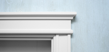 Close-up of a white doorframe showcasing intricate woodwork against a light blue textured wall. The image conveys simplicity and elegance.