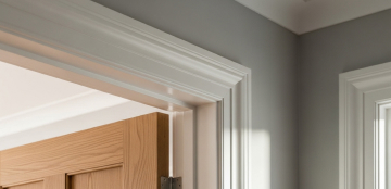 Close-up of a wooden door partially open, surrounded by white trim against a gray wall. Soft natural light enhances the calm, minimalist interior setting.