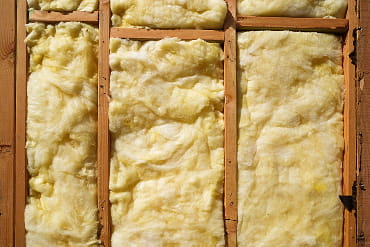 Close-up of yellow fiberglass insulation between wooden wall studs, highlighting its fluffy texture and effectiveness in thermal insulation.