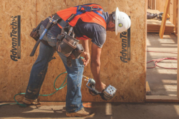 Construction worker in a tool belt and harness working on wall framing next to an AdvanTech sheathing panel.