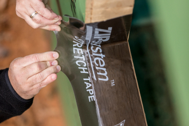 Installer applying ZIP System stretch tape over a sheathing seam by hand. Aerial view of a house under construction with yellow ZIP System sheathing installed on exterior wall framing.