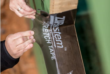 Hands applying ZIP System stretch tape over a flexible corner transition on framing lumber.
